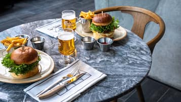 A dining table with two burgers, fries, and beer glasses.