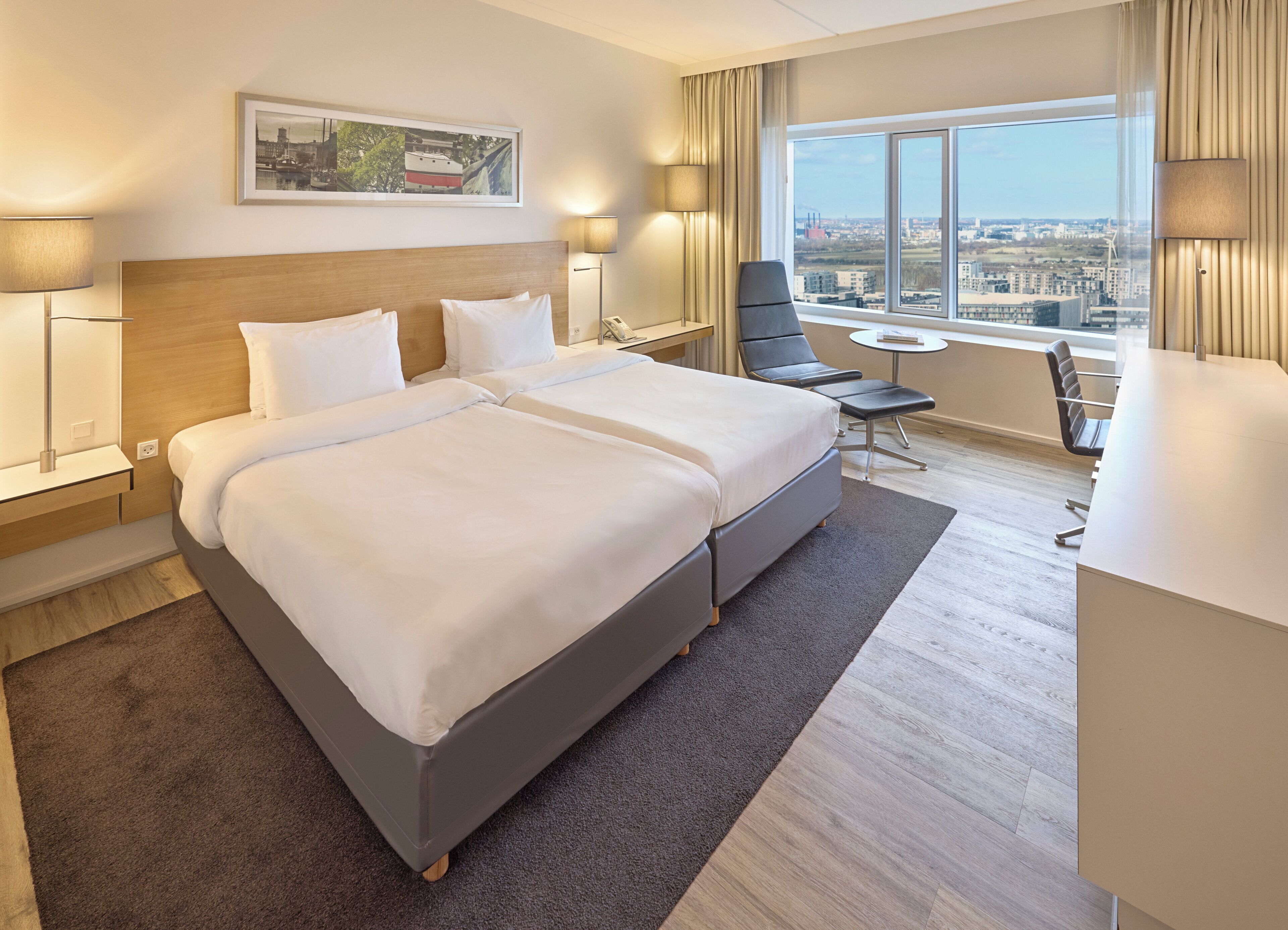 A hotel room with a large bed, a desk, a chair, and a view of the city.