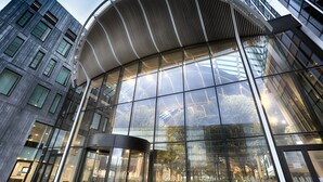 Un edificio moderno con facciata in vetro curvo e un ingresso ben visibile sormontato da una tettoia metallica.