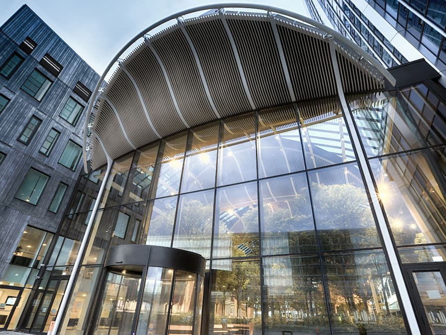 Een modern gebouw met een gebogen glazen gevel en een opvallende ingang met een metalen luifel.