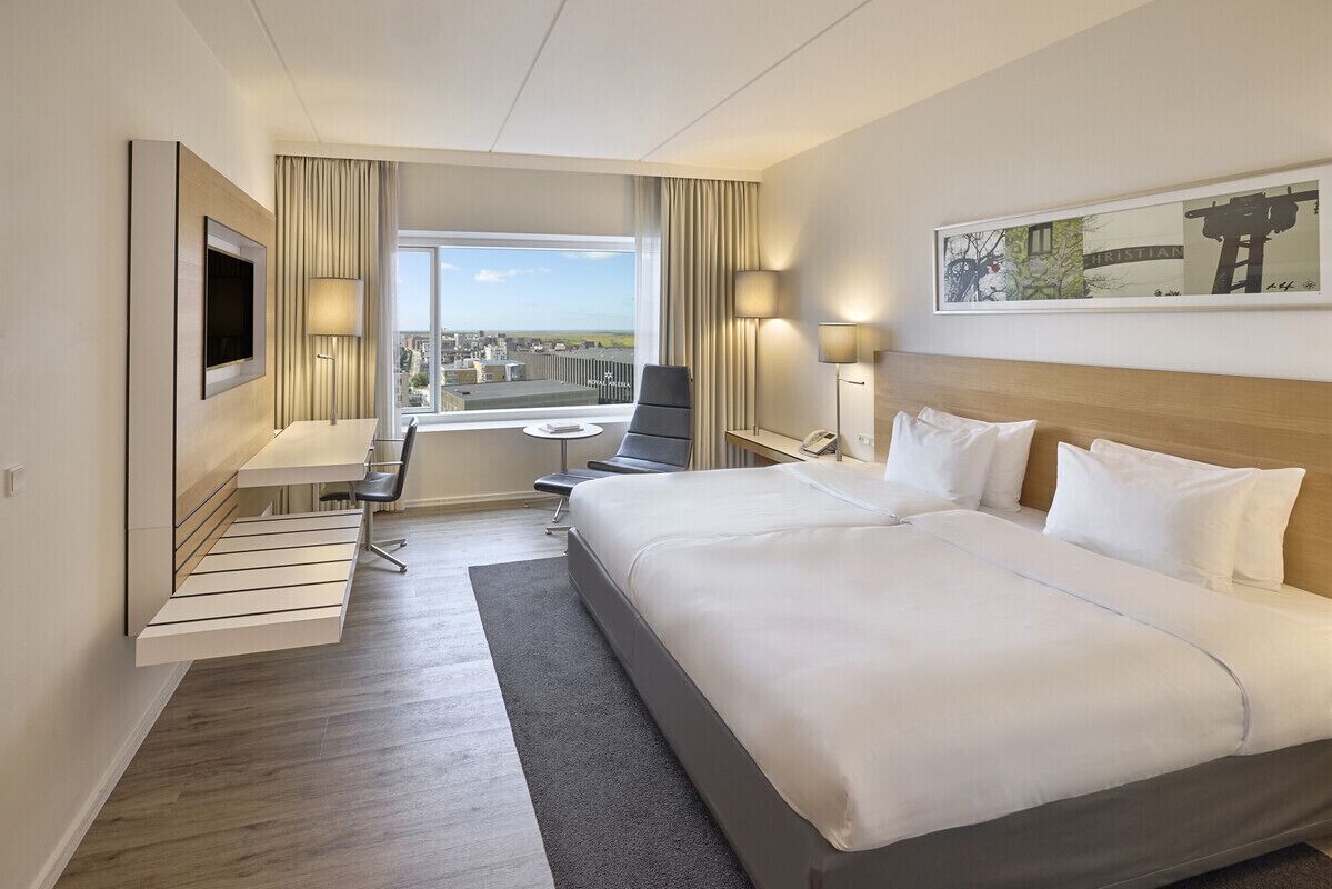 A hotel room with a large bed, a desk, a TV, and a window with a view.