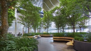 Un ampio atrio interno con soffitto alto, circondato da vegetazione rigogliosa e moderne zone relax.