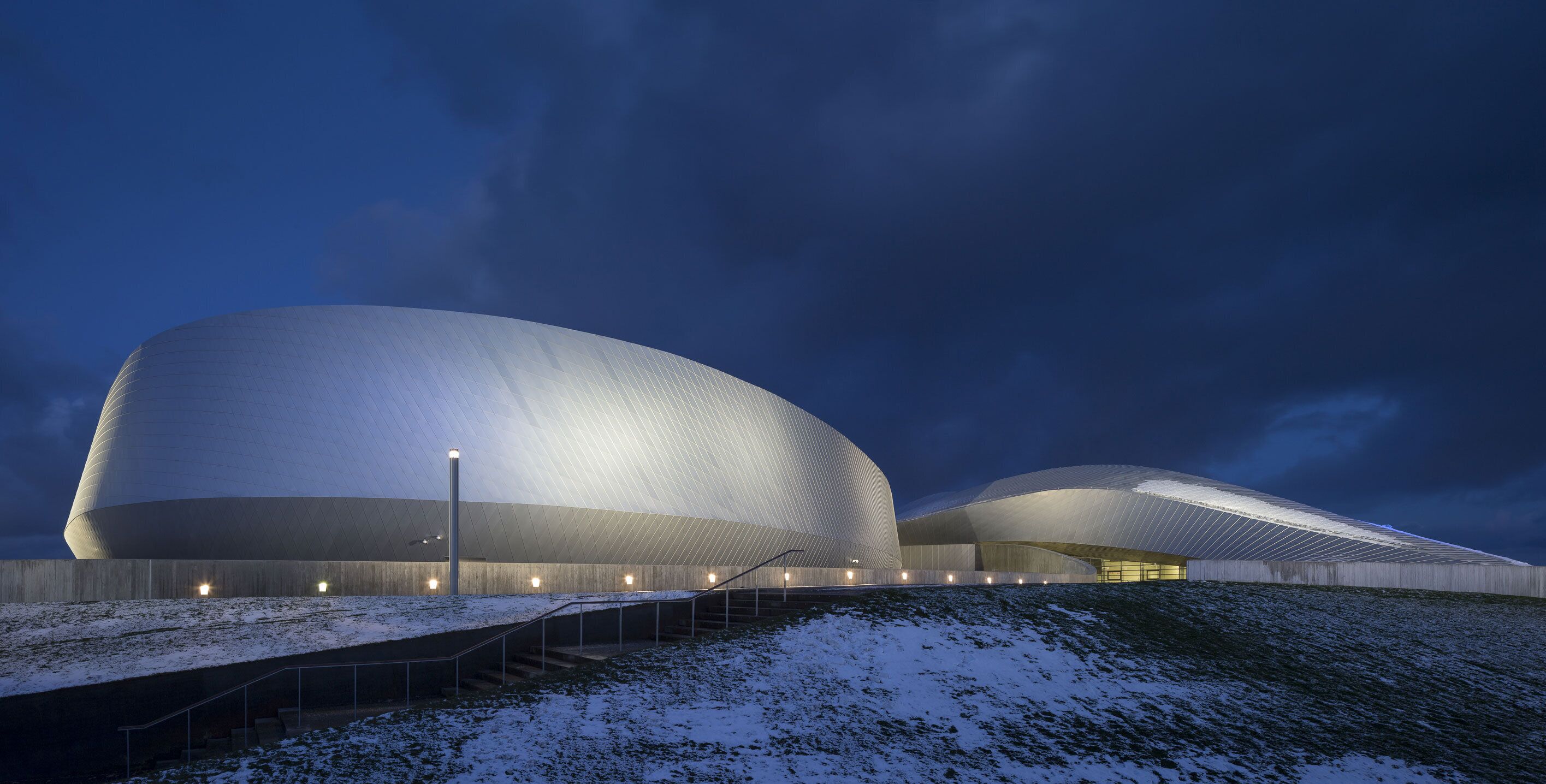 A modern architectural building with a unique curved design, featuring a series of steps leading up to the entrance.