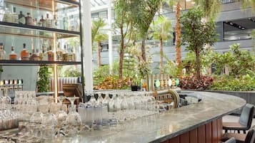 Zona de bar con una vitrina de botellas, un espacio de estar con un banco curvo y plantas de interior.