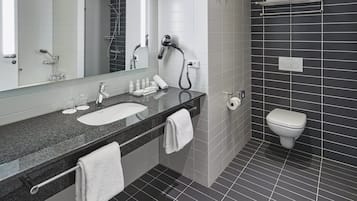 A modern bathroom with a large mirror, a vanity with a sink and towel rack, a hairdryer, and a toilet.