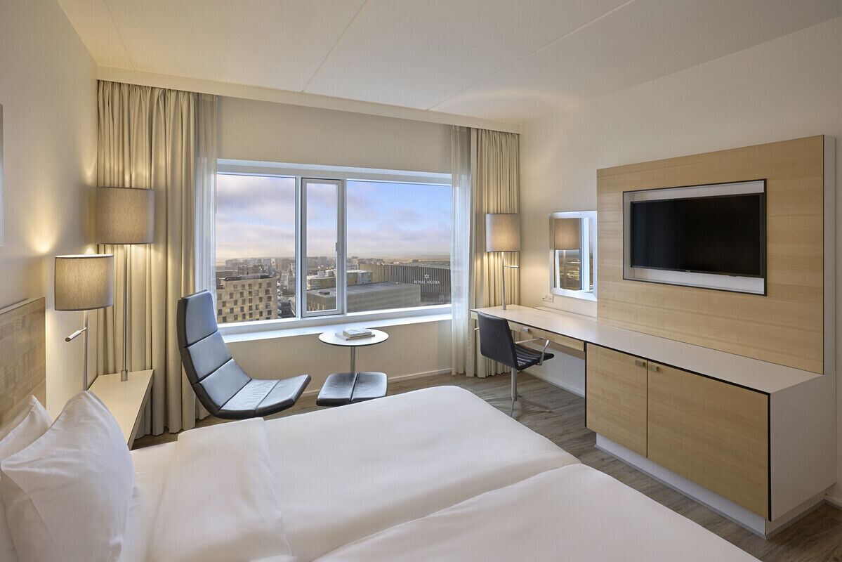 Habitación de hotel con cama, escritorio, silla, televisor y ventana con vista a la ciudad.