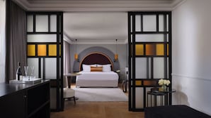 Una habitación de hotel con una cama grande, un escritorio, una silla, una mesita con un jarrón y un armario.