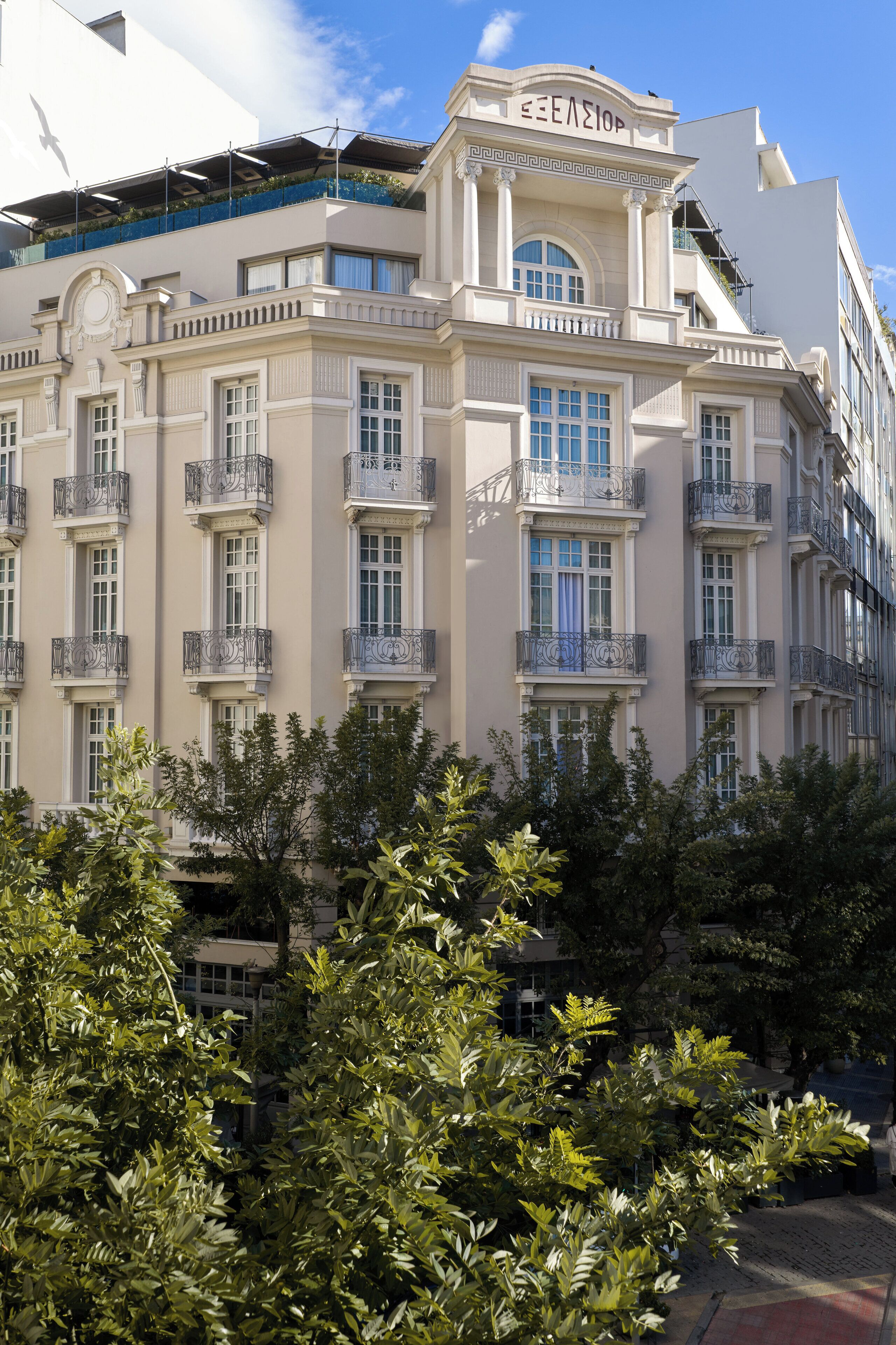 A multi-story building with balconies and large windows, surrounded by trees.