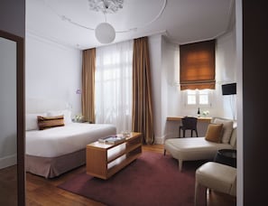 A modern hotel room with a bed, a desk, a chair, and a sofa.