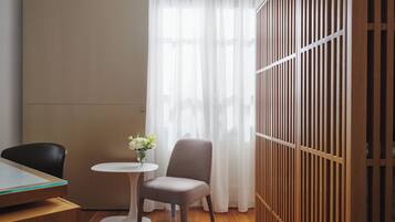 A room with a wooden floor, a round table with a vase of flowers, a chair, and a partition with vertical slats.
