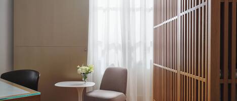 Una habitación con piso de madera, una mesa redonda con un florero, una silla y un separador con listones verticales.