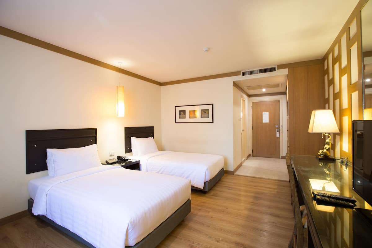 Een hotelkamer met twee bedden, een bureau met een lamp, een televisie en een ingelijst kunstwerk aan de muur.
