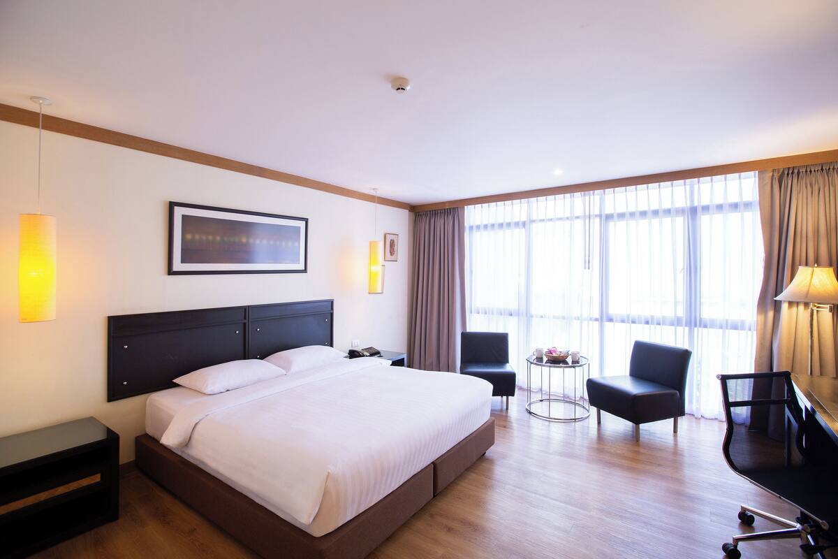 Een hotelkamer met een groot bed, een bureau, twee stoelen en een raam met gordijnen.