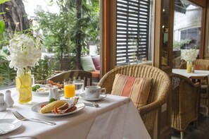 A dining table set with breakfast items, a wicker chair, and a view of greenery outside.