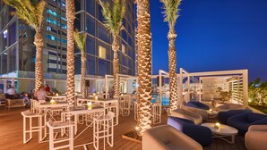 An outdoor seating area with tables and chairs, palm trees, and a pool in the background. - Media One Hotel Dubai, WorldHotels Crafted (Dubai)