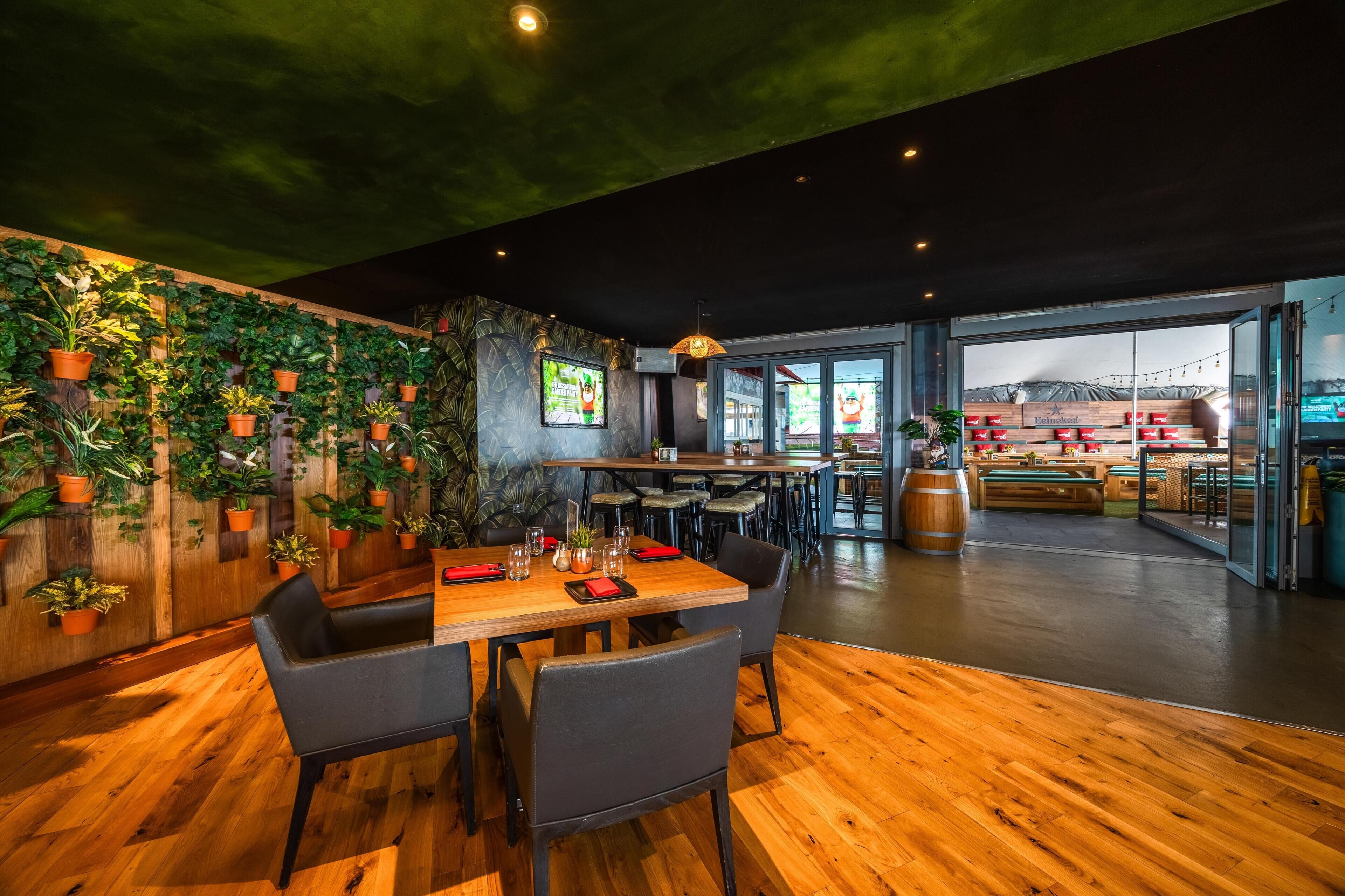 Un restaurante con suelo de madera, una mesa preparada para dos personas y una pared decorada con plantas en macetas.