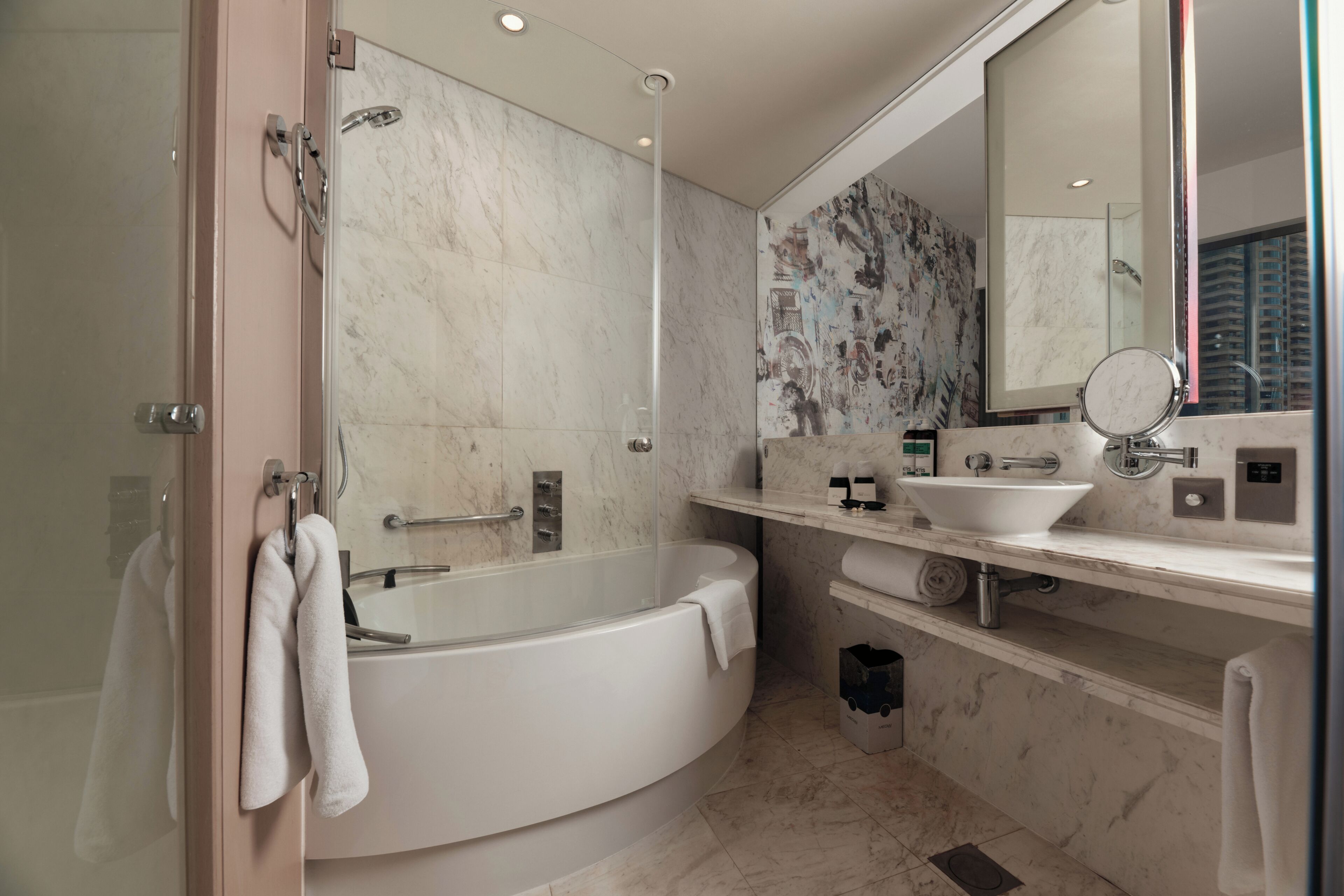 A modern bathroom with a freestanding bathtub, a large mirror, and a marble wall.