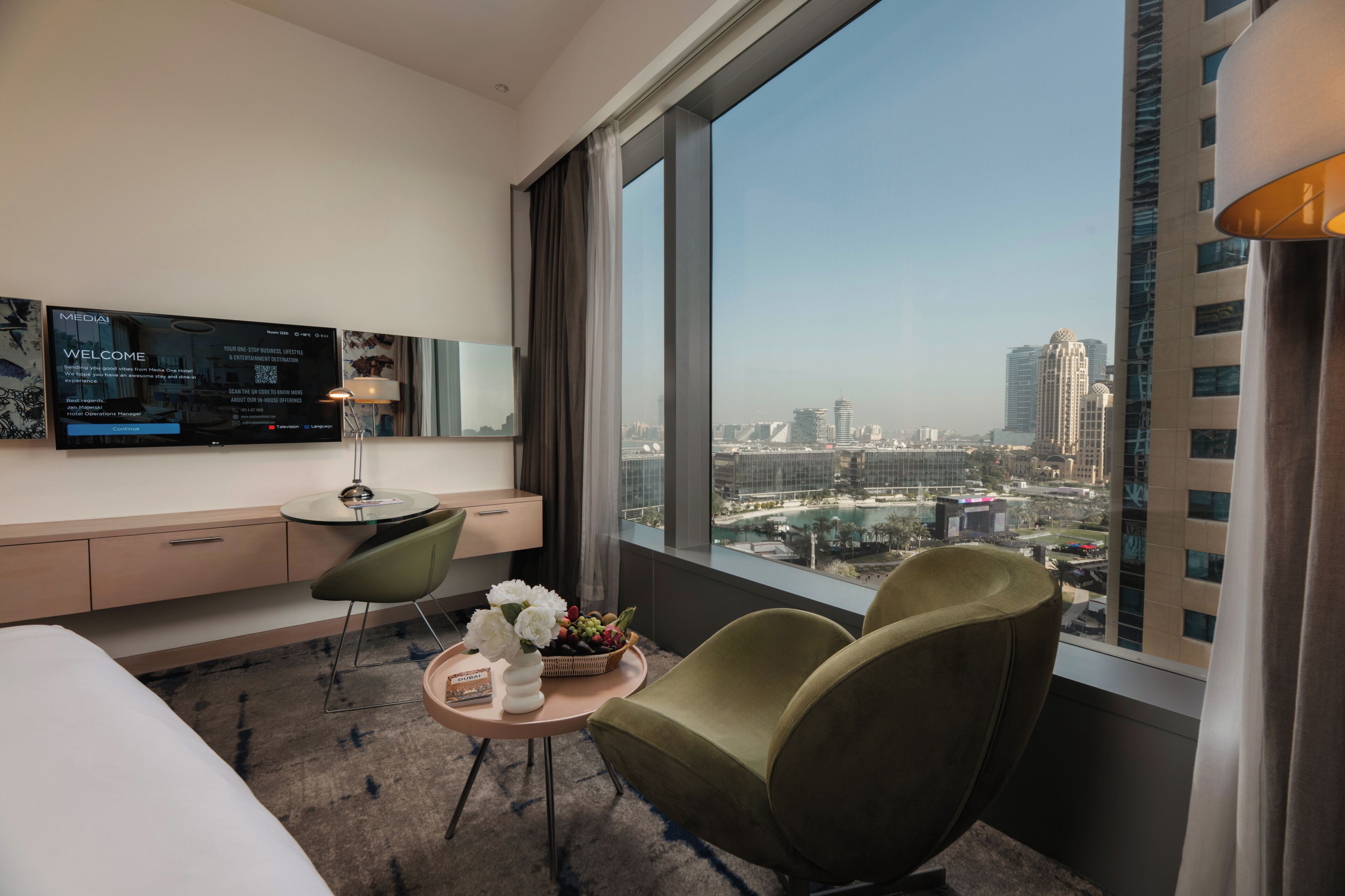A hotel room with a large window, a desk with a computer, a bed, and a chair.