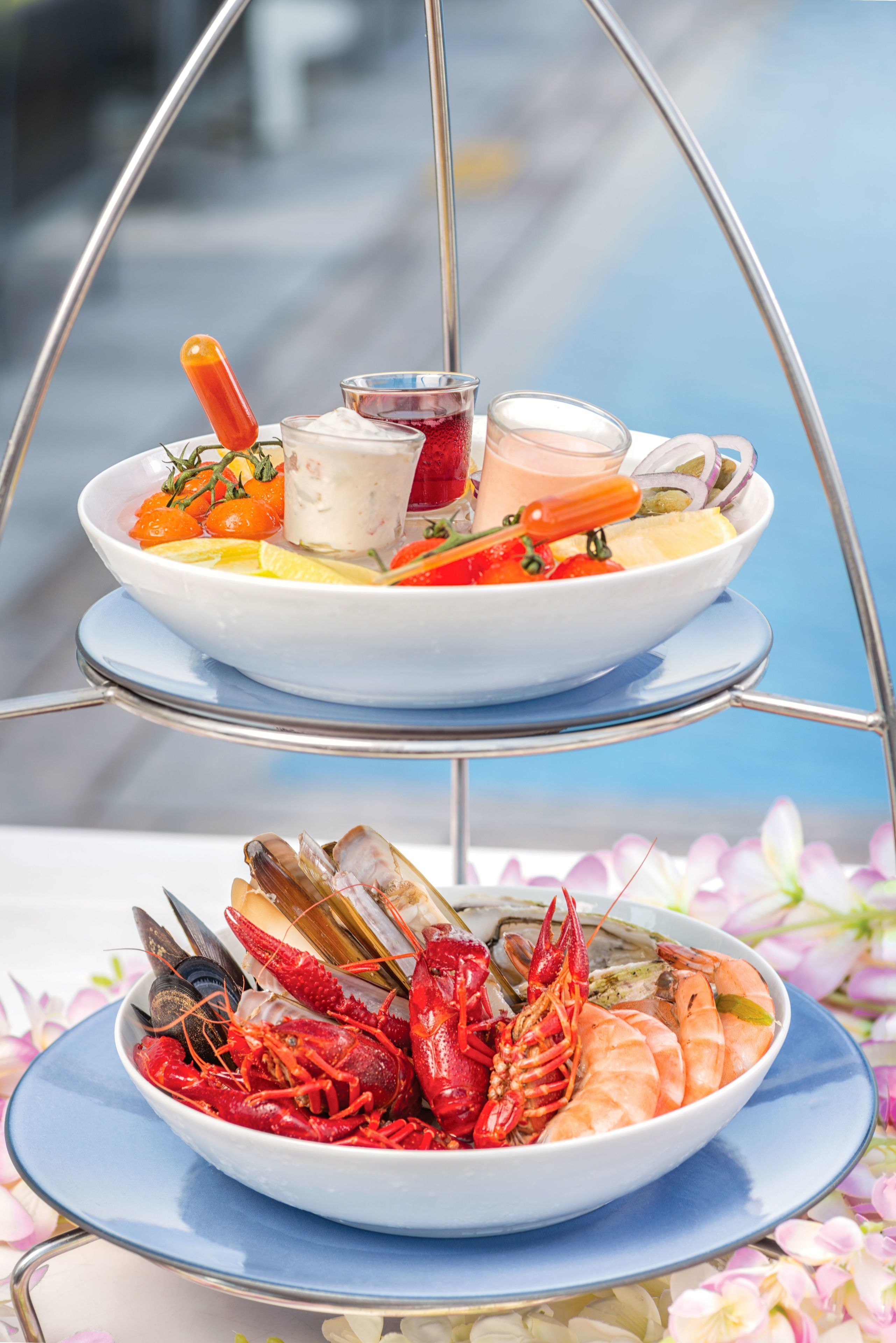 Una bandeja de mariscos con diversos mariscos y un recipiente pequeño con salsa, sobre un soporte metálico.
