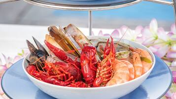 Una bandeja de mariscos con diversos mariscos y un recipiente pequeño con salsa, sobre un soporte metálico.