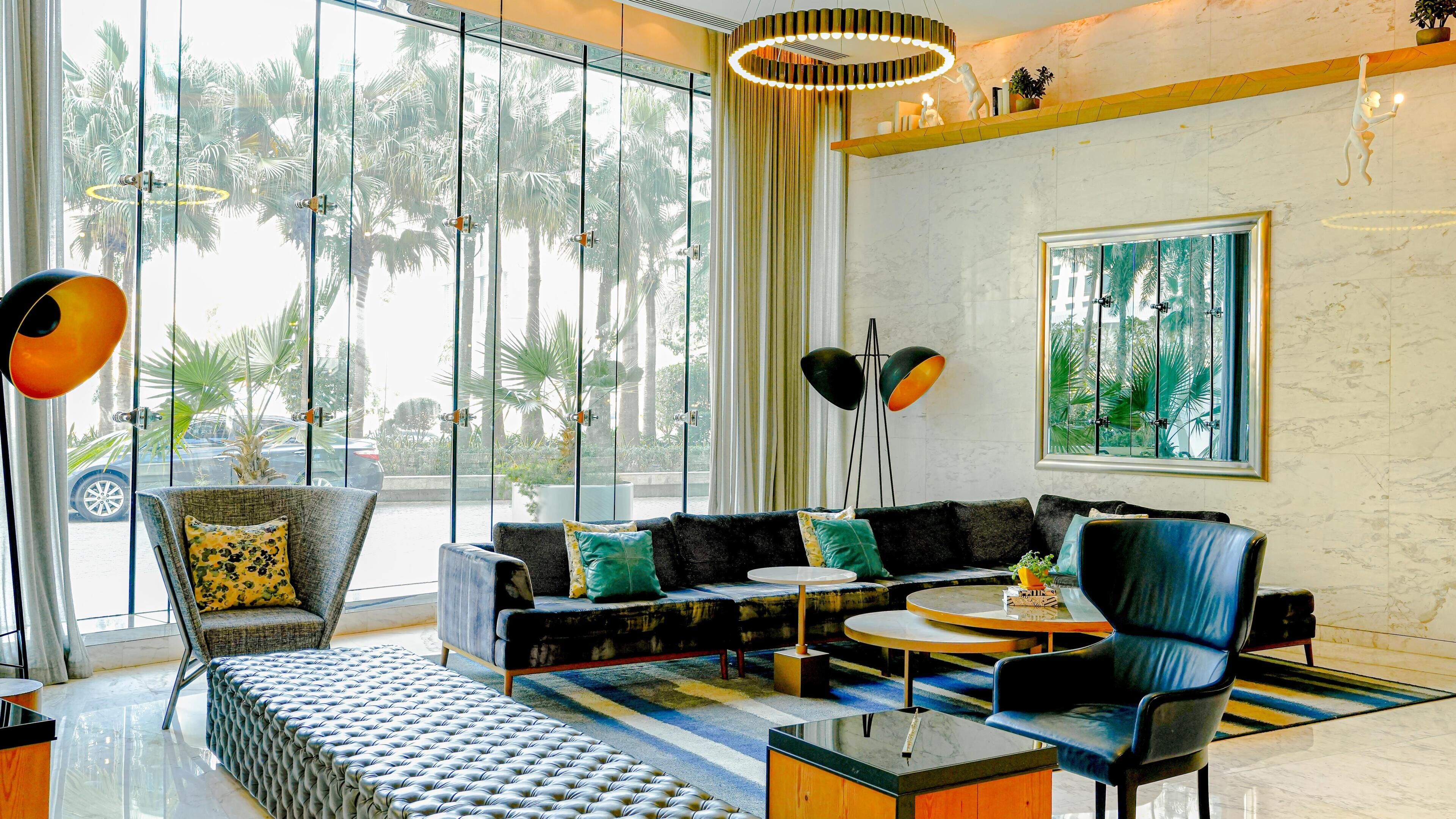A modern living room with a sofa, armchairs, a coffee table, and a large window with a view of palm trees.