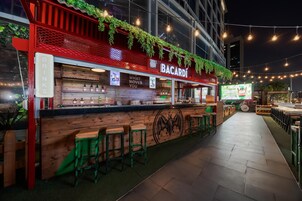 Zona de bar al aire libre con un cartel de Bacardi, mostrador de bar de madera, taburetes verdes y un camino que conduce a más asientos.