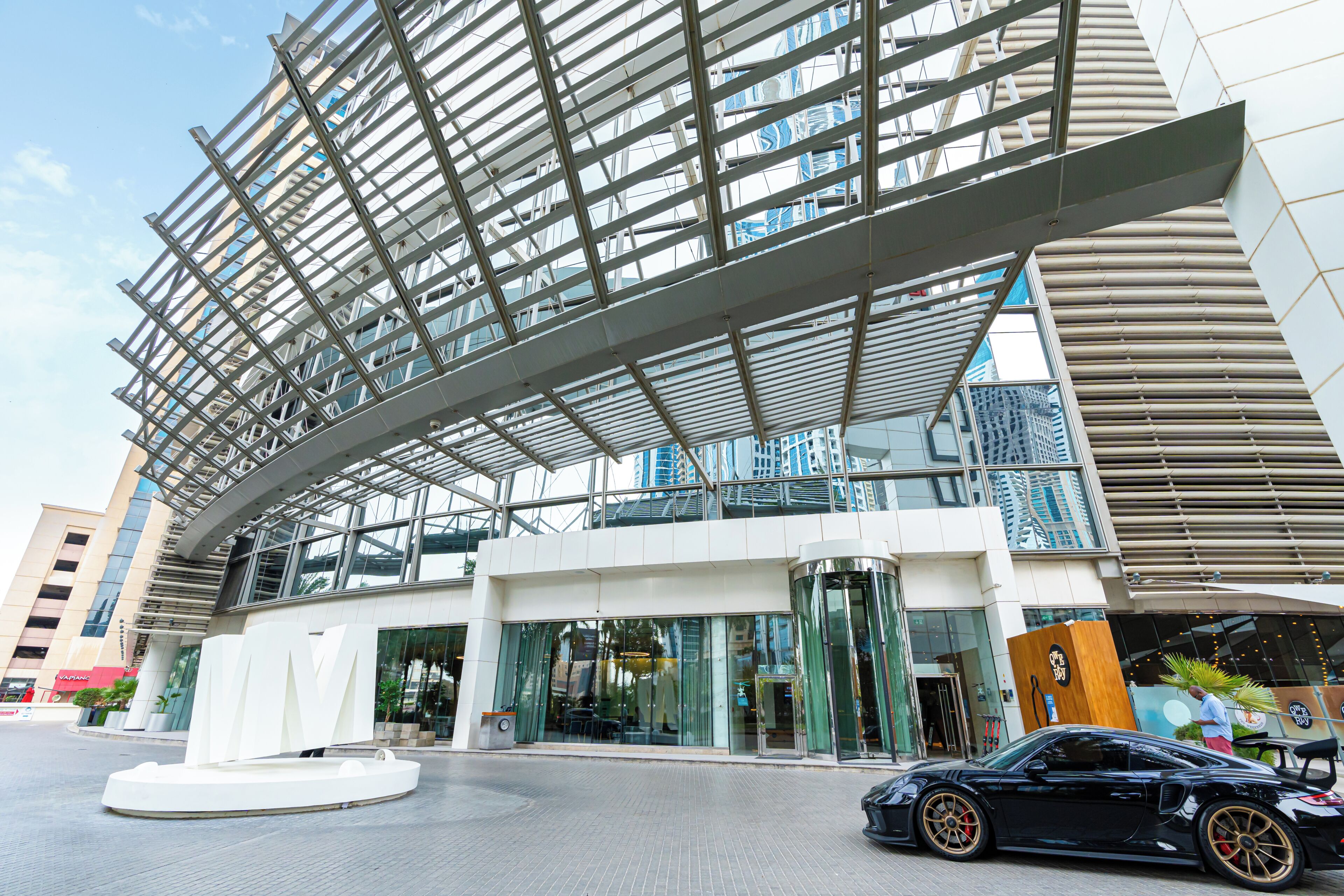 A modern building with a glass facade, a prominent entrance with a revolving door, and a black car parked in front.