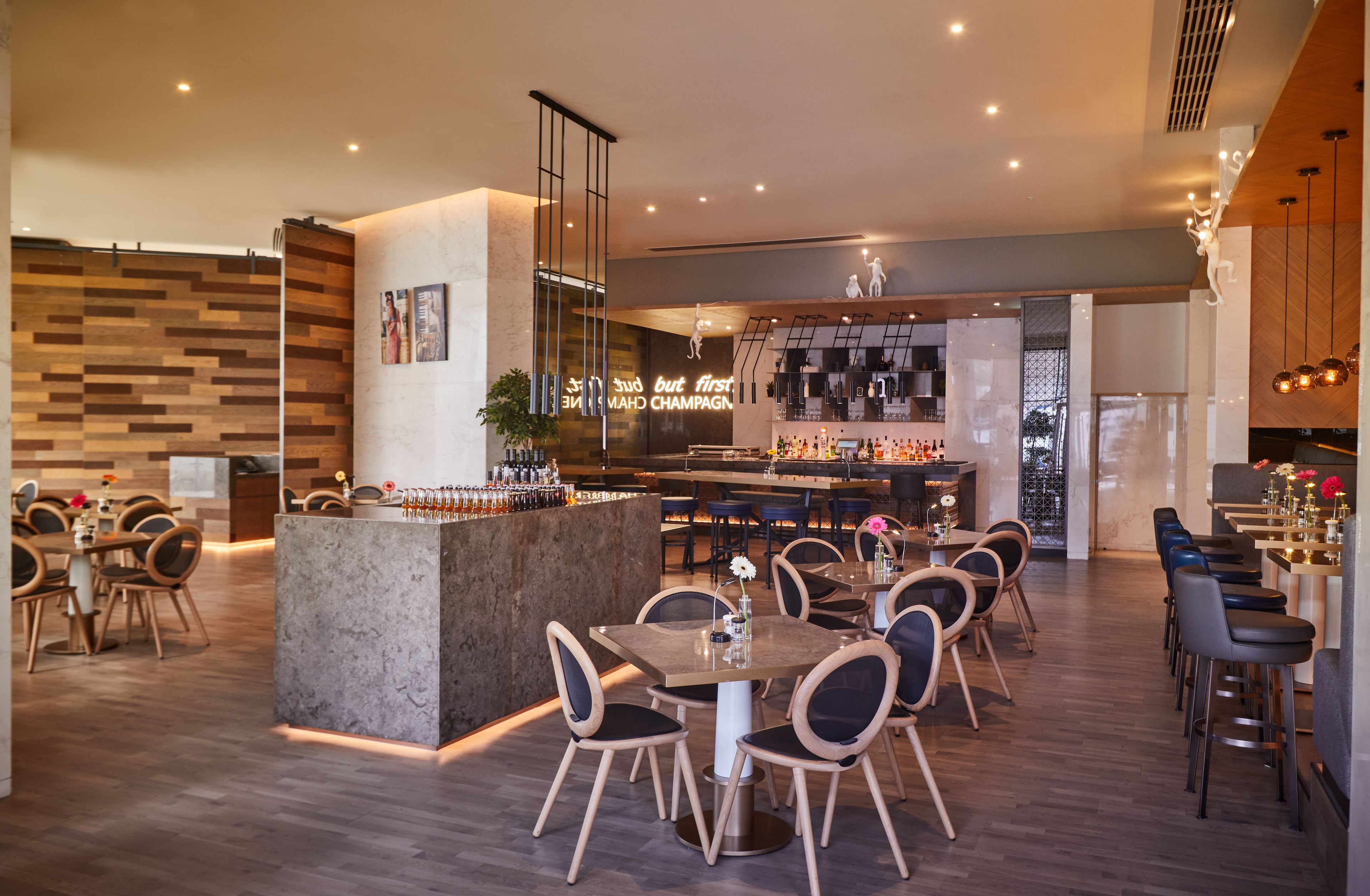 Un restaurante moderno con zona de bar, suelo de madera y una isla central con asientos.
