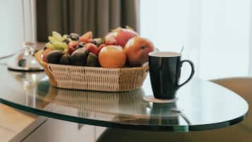Una mesa con cubierta de vidrio, una cesta de fruta, una taza de café y una lámpara.