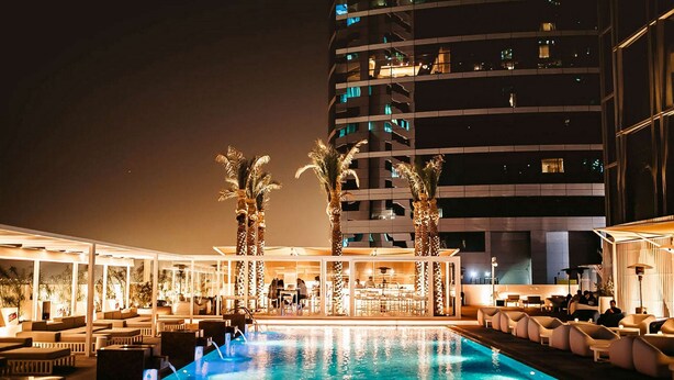 A nighttime pool area with lounge chairs and palm trees, adjacent to a high-rise building with illuminated windows. - Media One Hotel Dubai, WorldHotels Crafted (Dubai)