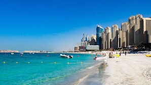 A beach with clear turquoise water, a sandy shore, and a city skyline in the background. - Media One Hotel Dubai, WorldHotels Crafted (Dubai)