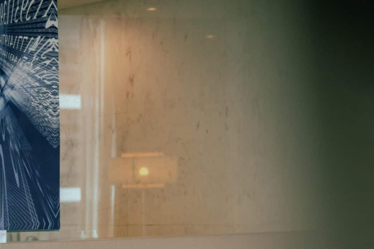A hotel room with a neatly made bed, a rolled towel, and a wall with a patterned tapestry.