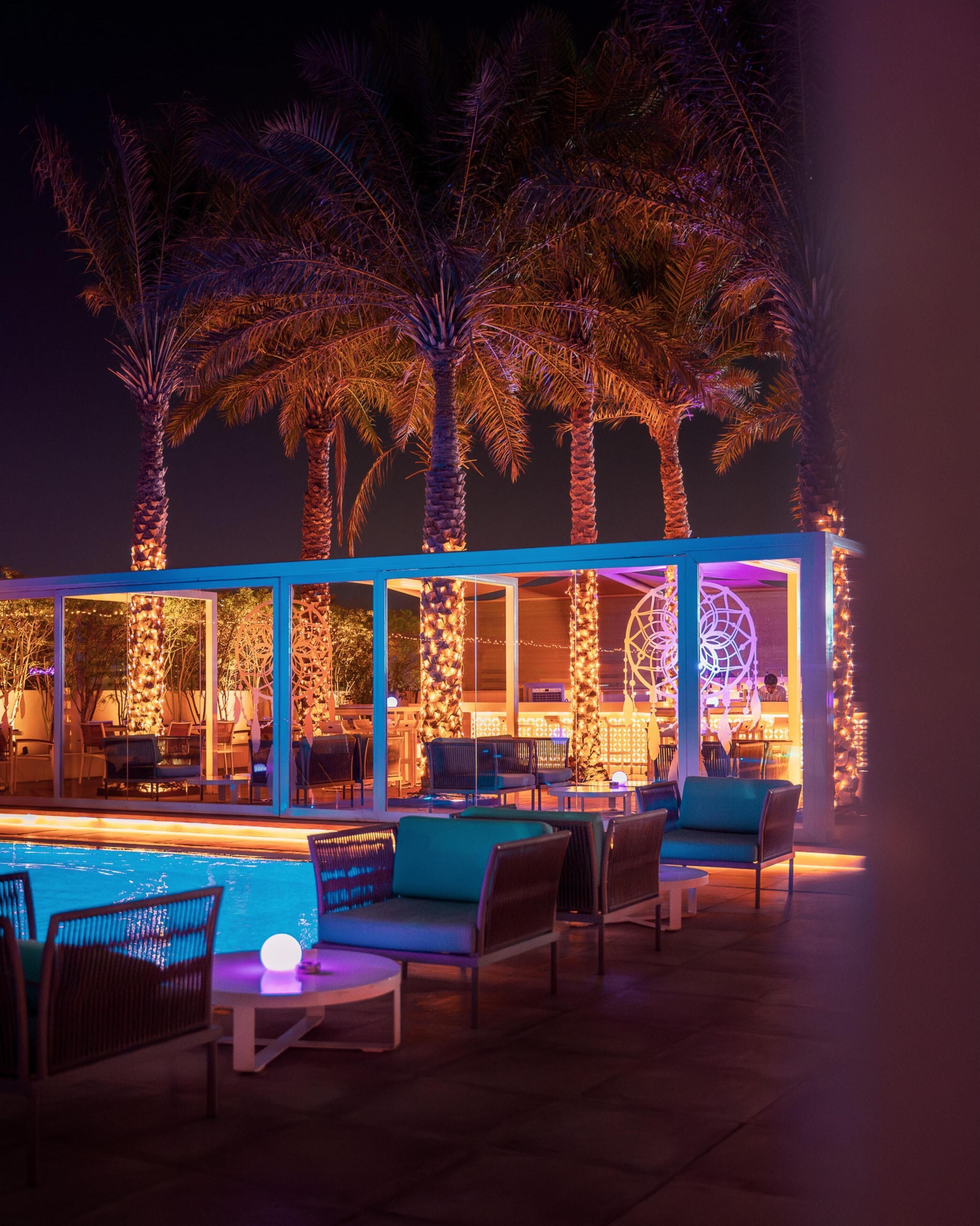 A poolside area with lounge chairs and a bar area with illuminated columns.