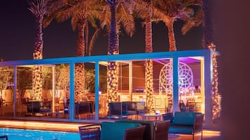 A poolside area with lounge chairs and a bar area with illuminated columns.