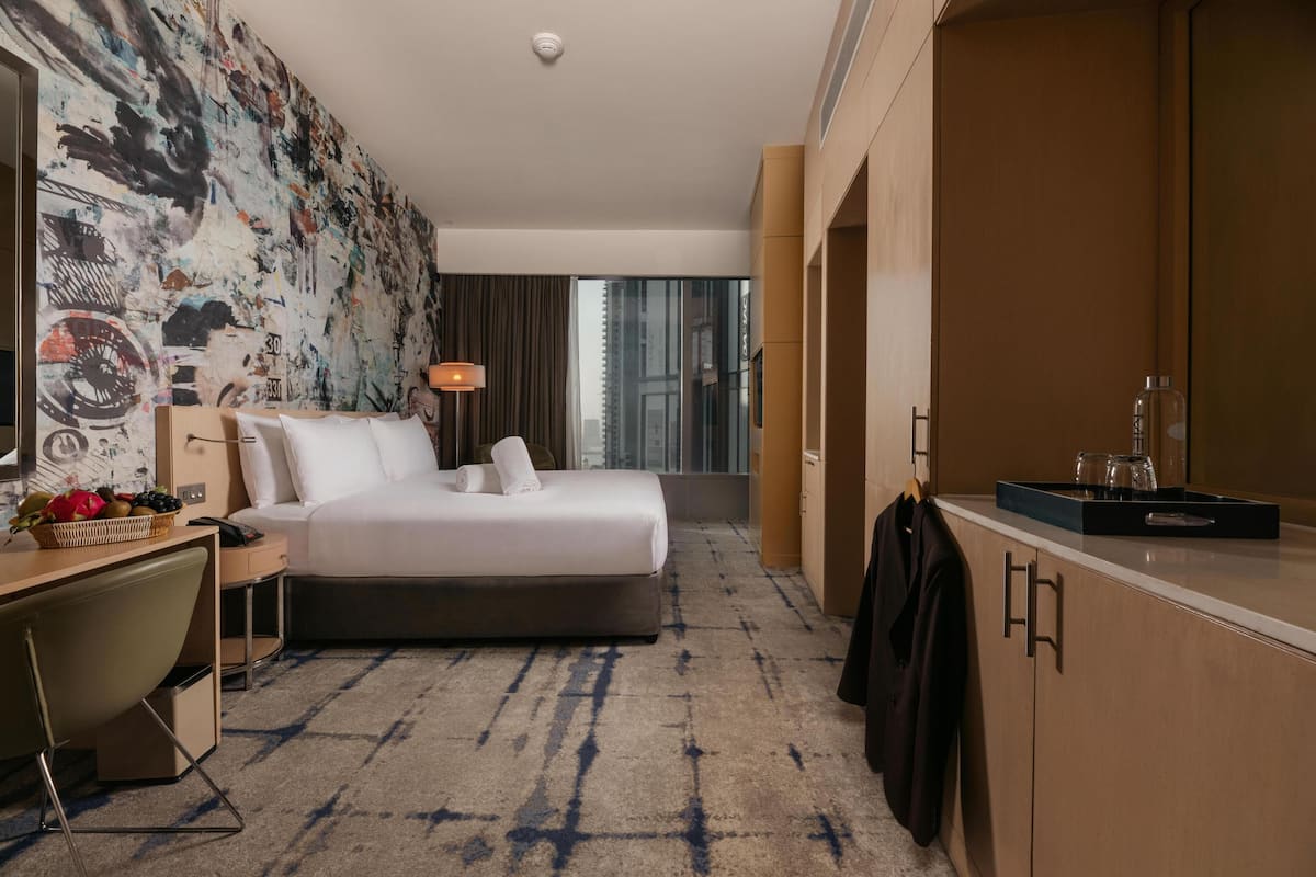 A hotel room with a bed, desk, chair, and a large window.