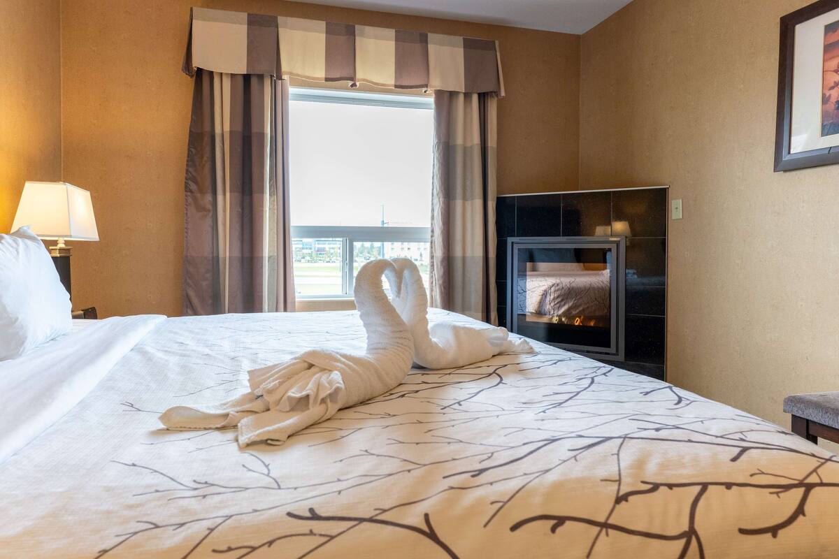 A hotel room with a bed, a TV, a fireplace, and a window with curtains.