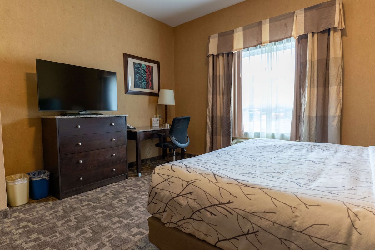 A hotel room with a bed, a desk with a chair, a television, and a window with curtains.