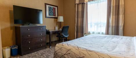 A hotel room with a bed, a desk with a chair, a television, and a window with curtains.