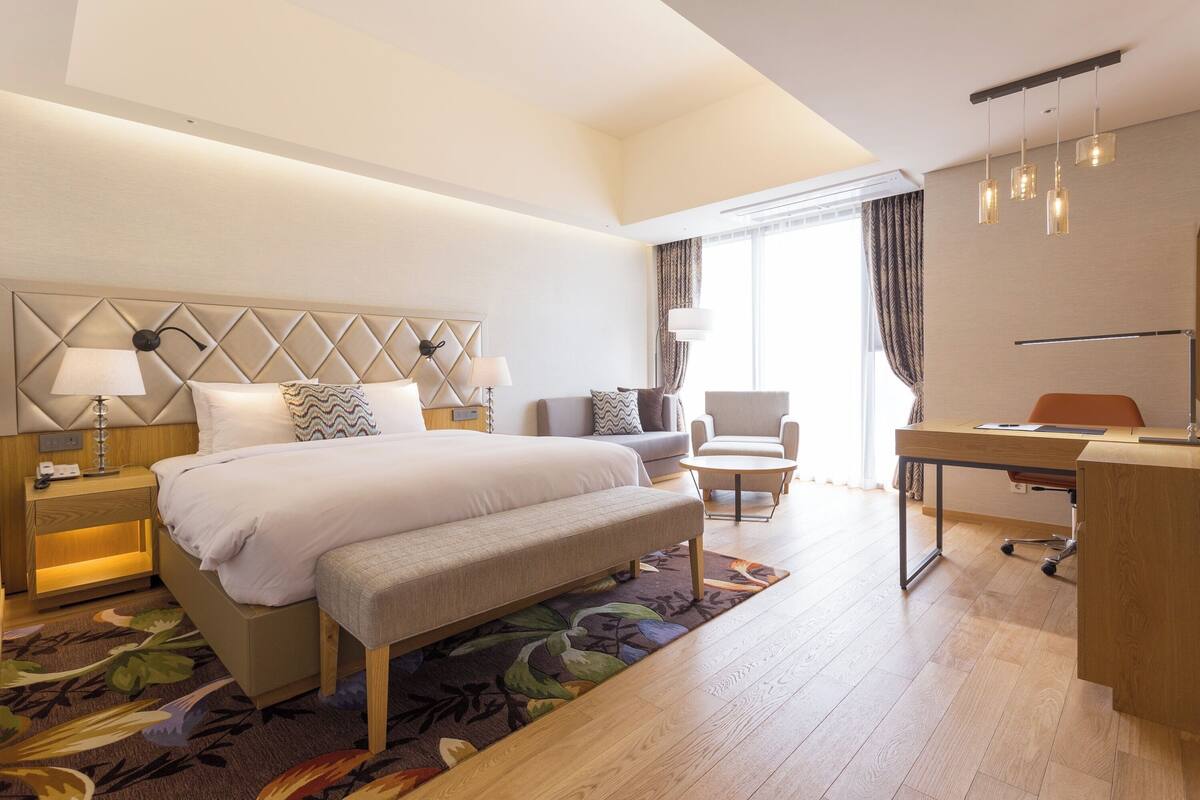 A modern hotel room with a large bed, bedside tables, a desk, and a chair.