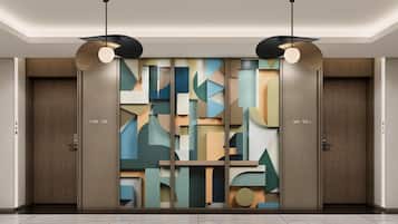 Een moderne hotellobby met een geometrisch wandontwerp, twee houten deuren met kamer nummers, en hanglampen.