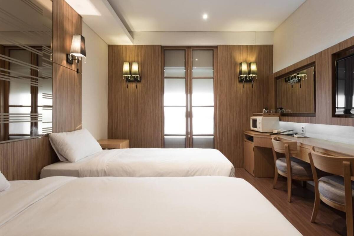 A hotel room with two beds, a desk with a chair, a microwave, and a large mirror.