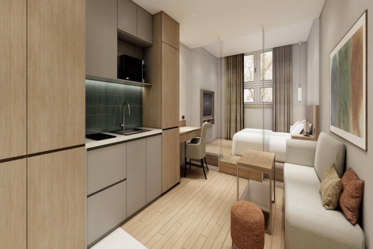 A modern hotel room with a kitchenette, a bed, a desk, and a sofa.