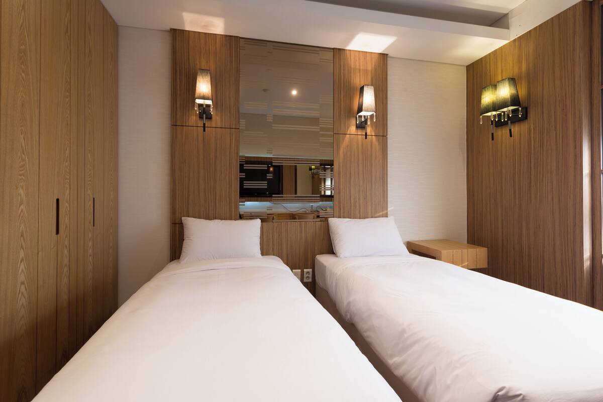 A hotel room with two beds, wooden paneling, a large mirror, and wall-mounted lamps.