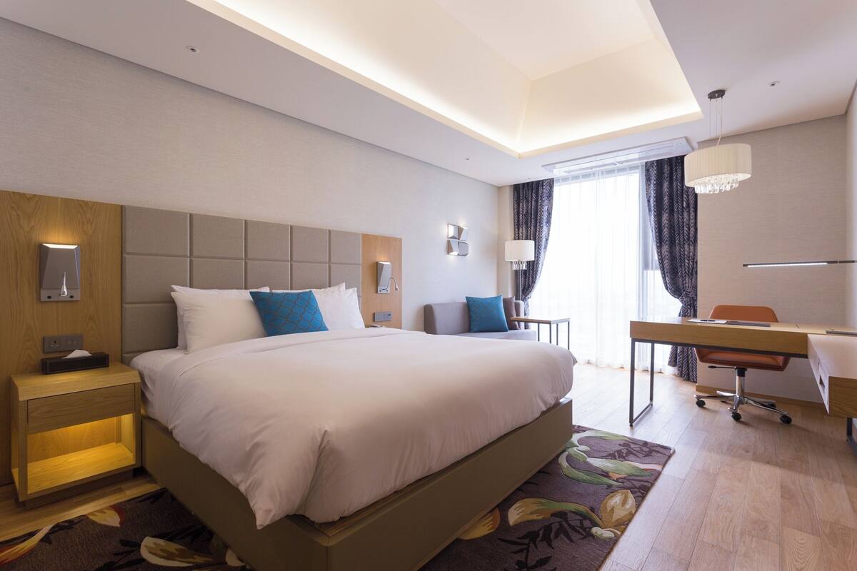 A modern hotel room with a large bed, bedside tables, a desk, and a chair.