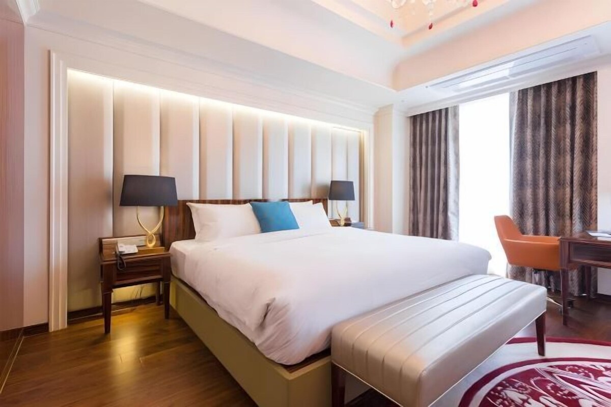 Una camera d'albergo con un letto grande, comodini con lampade, una scrivania e una sedia.