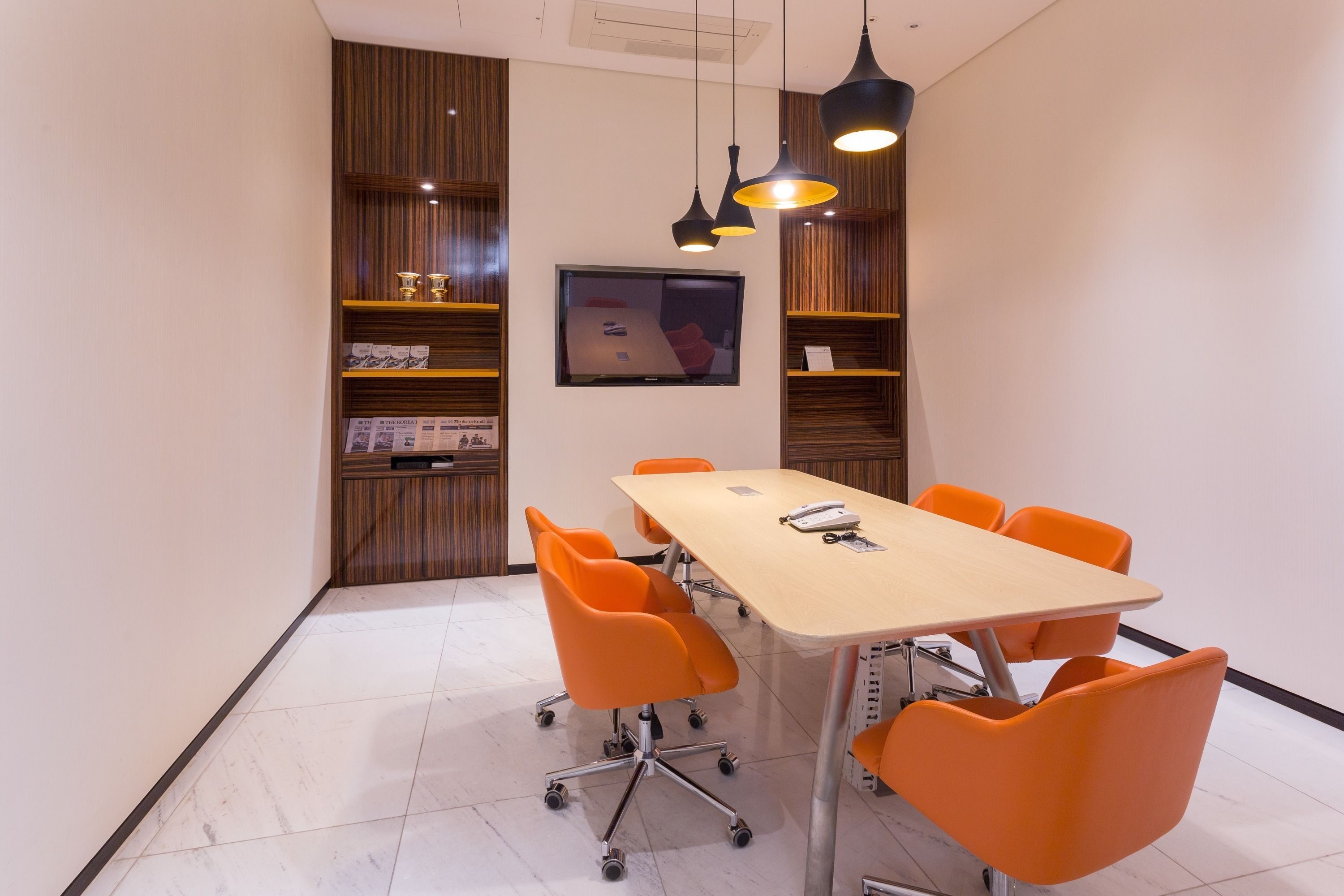 A conference room with a long table, six orange chairs, and a television on the wall.