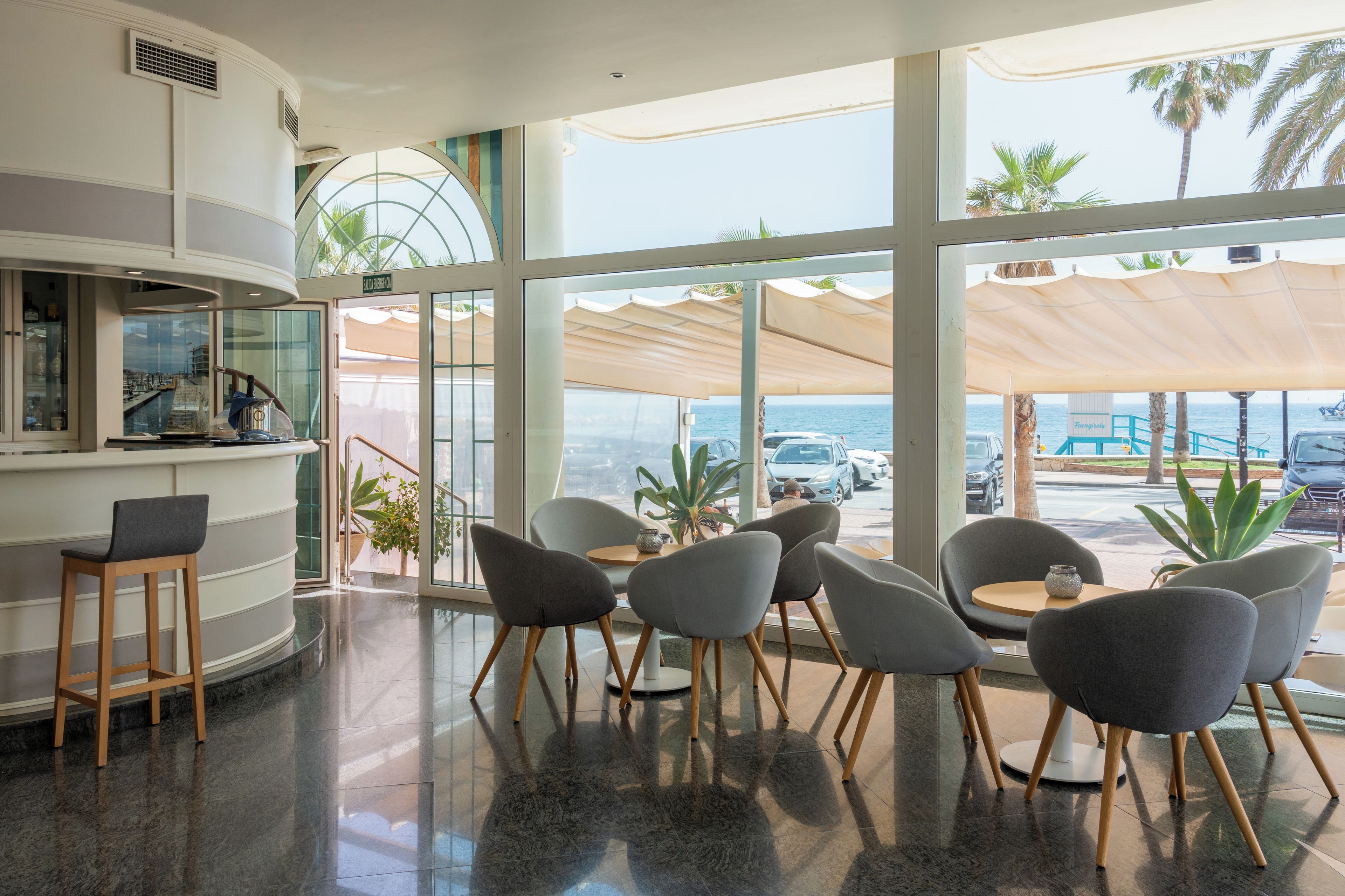 A modern interior with a bar area, seating, and large windows offering a view of the sea.