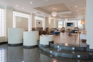 A hotel lobby with a reception desk, seating area, and a staircase leading to another level. - Hotel Villa de Laredo (Fuengirola)