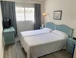 Une chambre d’hôtel avec deux lits, un téléviseur posé sur une table d’appoint, une lampe de chevet et un tableau au mur.