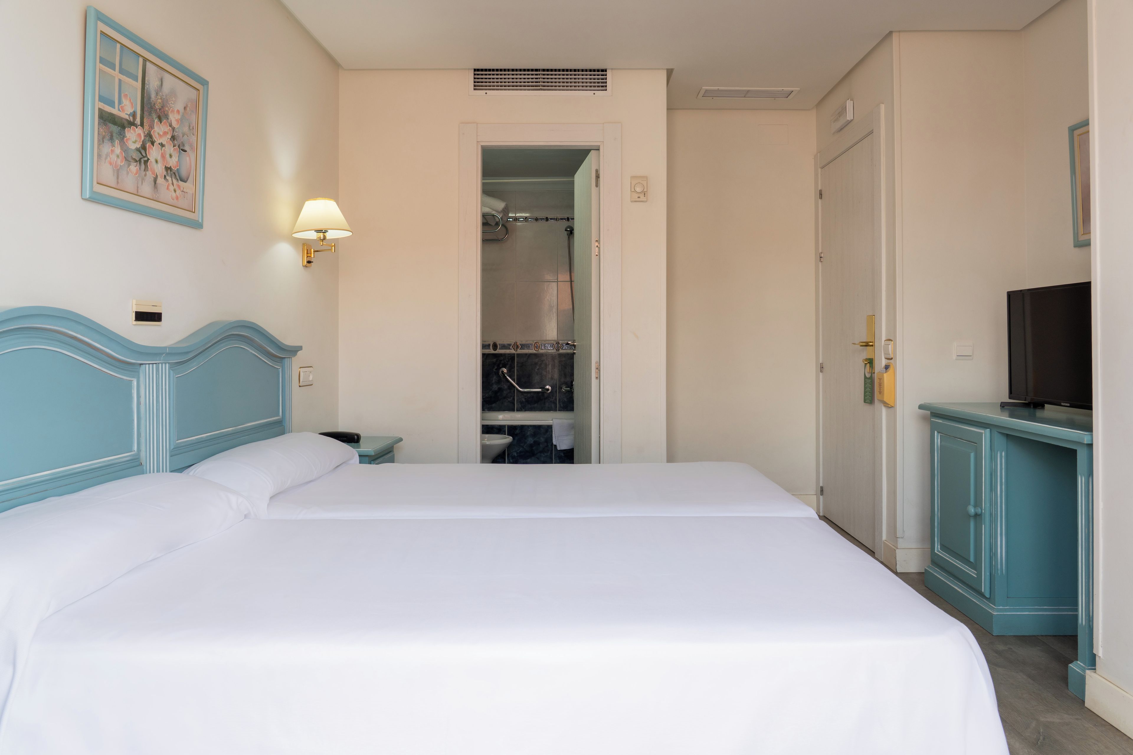 A hotel room with a large bed, a television, a wardrobe, and a bathroom visible through an open door.